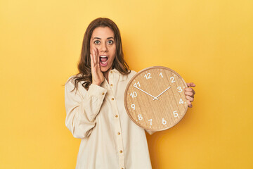 Wall Mural - Woman holding clock on yellow backdrop is saying a secret hot braking news and looking aside