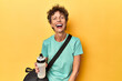 © Asier - Sportswoman with gym bag & water on yellow studio laughing and having fun.