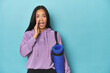 Filipina athlete with yoga mat on blue is saying a secret hot braking news and looking aside