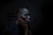 © Road Red Runner - A portrait capturing a young black African man with his hands on his face, in a prayerful position, inside a dimly lit room.