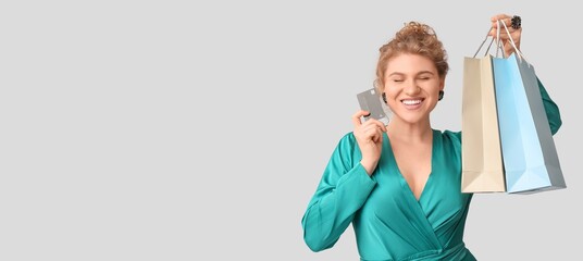 Wall Mural - Happy young woman with credit card and shopping bags on light background with space for text