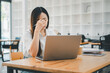 © Mongta Studio - Business and technology concept, A stressed young female professional is rubbing her forehead while looking at a laptop screen in a modern workspace setting.