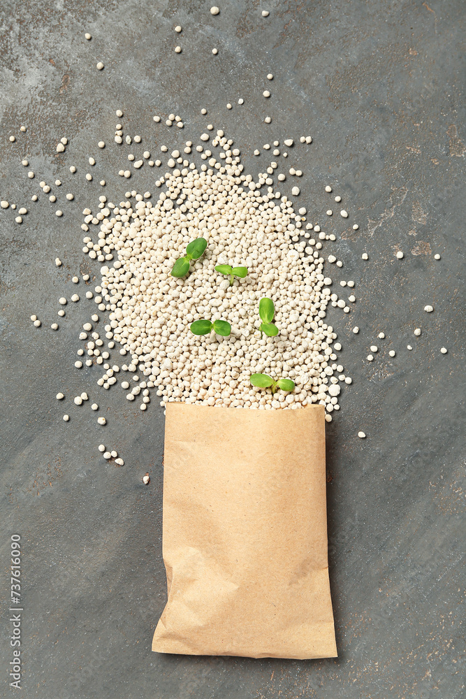 Paper bag with granular fertilizer and seedlings on grey grunge background