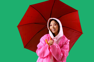 Sticker - Young Asian woman in pink hoodie and raincoat with umbrella on green background