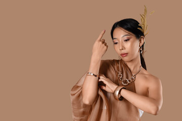 Young Asian woman with jewelry and fabric on beige background