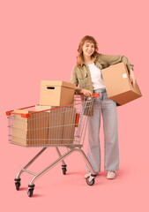 Sticker - Young woman with cardboard boxes in shopping cart on pink background