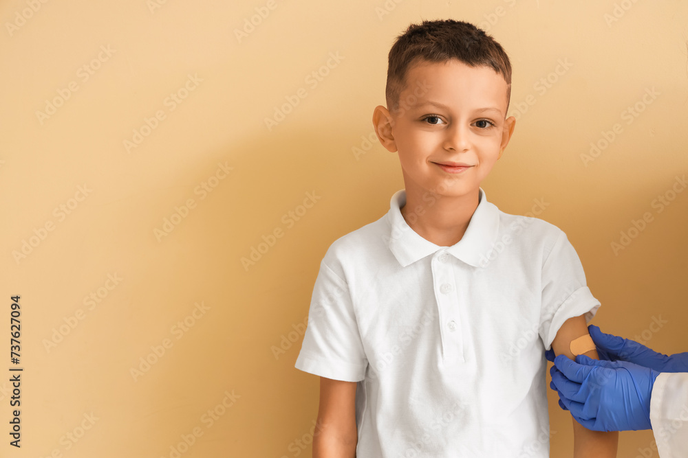 Little boy receiving plaster from doctor after vaccination on beige background