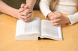 © New Africa - Girl and her godparent praying over Bible together at table indoors, closeup