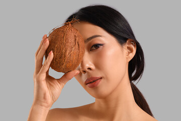 Wall Mural - Pretty young Asian woman with coconut on grey background