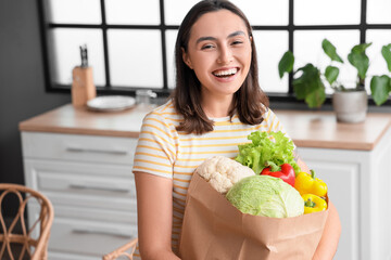 Wall Mural - Young woman with paper bag of fresh vegetables in kitchen