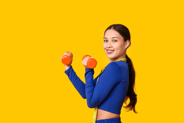 Poster - Young woman in sportswear, with measuring tape and dumbbells on yellow background. Weight loss concept