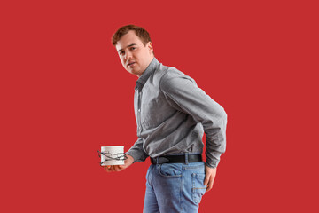 Poster - Young man with barbed toilet paper on red background. Hemorrhoids concept