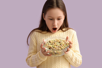 Canvas Print - Shocked little girl holding bowl with cereal rings on lilac background