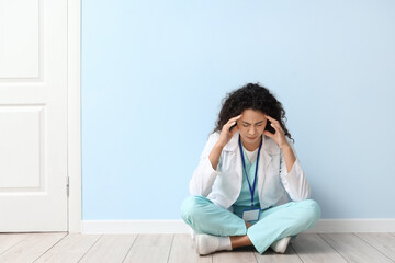 Wall Mural - stressed female African-American medical intern sitting near blue wall