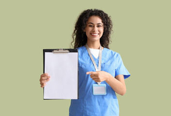 Wall Mural - Female African-American medical intern pointing at clipboard on green background