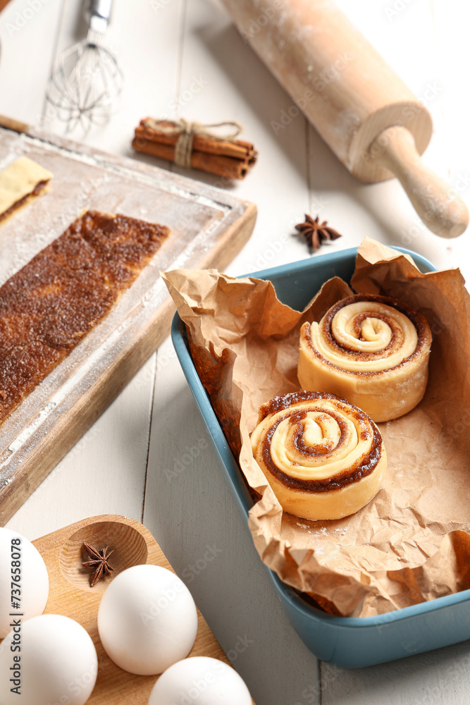 Ingredients and kitchen utensils for cooking cinnamon buns on white wooden background