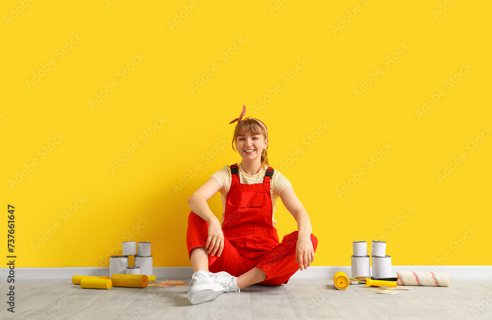 Female decorator with paint rollers and cans sitting during repair in room