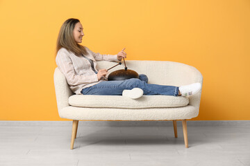 Poster - Beautiful mature woman with sticks playing glucophone and sitting on sofa near yellow wall