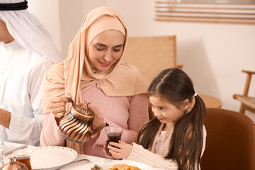 Wall Mural - Happy Muslim mother pouring tea for her little daughter at family dinner. Ramadan celebration