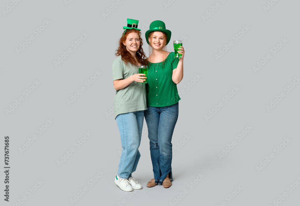 Young redhead women with beer on light background. St. Patrick's Day celebration
