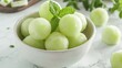 A bowl containing refreshing honeydew melon balls on a plain white table