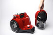 Hand holding a modern red vacuum cleaner on a white background