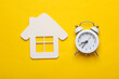 White wooden figurine of house and alarm clock on yellow background