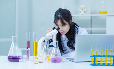 Asian young woman female laboratory professional scientist concentrated in a white lab coat, protective eyeglasses making test tubes looking microscope research medicine experiments in chemical lab.