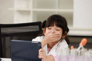 Asian little girl scientist in lab coat reading tablet computer for data learning science at chemical laboratory study room. Education research and development concept learning for kids.