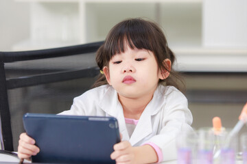 Wall Mural - Asian little girl scientist in lab coat reading tablet computer for data learning science at chemical laboratory study room. Education research and development concept learning for kids.