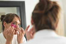 Caucasian Woman Applies A Pink Eye Mask At Home