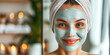 Beautiful smiling young woman with towel wrapped around her head applying face mask in the bathroom. Young woman with clay face mask, Cosmetic procedures, beauty and skin care