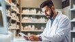 © liliyabatyrova - A handsome bearded young Male pharmacist is sitting at a table with a tablet in a pharmacy. Medical worker, pharmaceutical business, Healthcare concepts.