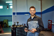 © bnenin - Portrait of a smiling mechanic, posing for the camera while holding a digital tablet, at his auto service.