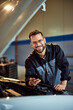 © bnenin - A portrait of a smiling mechanic man, looking at the camera, holding a mobile phone.