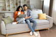 © Home-stock - Planning vacation. Happy young indian couple searching tour online, using laptop computer, sitting on couch in cozy living room interior at home, free space