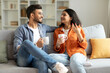 © Home-stock - Loving hindu spouses drinking coffee and chatting while sitting on sofa at home, enjoying spending time together on weekend. Happy romantic relationship