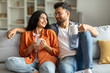 © Home-stock - Weekend morning. Happy hindu spouses enjoying hot coffee and talking, sitting on sofa, holding cups with hot beverages. Domestic lifestyle