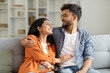 © Home-stock - Indian lovers couple enjoying time together at home, happy man and woman embracing and talking, sitting on couch in living room