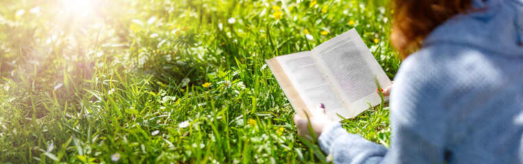 Young woman lying on the field and reading a book.