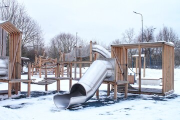 Wall Mural - Wooden playground made of natural eco-friendly material in public city park with snow at winter time. Modern safety children outdoor equipment. Winter activities. Children rest and games on open air