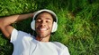 Young man listening to the music via headphones while having rest on the lawn. Tunes and tranquility on the green. Harmony