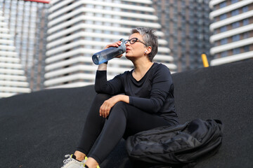 Sticker - A healthy Caucasian woman takes a break in the park, staying hydrated with a refreshing water bottle.