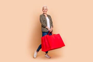 Poster - Full size photo of pretty senior female hold shopping bags look empty space wear trendy khaki outfit isolated on beige color background