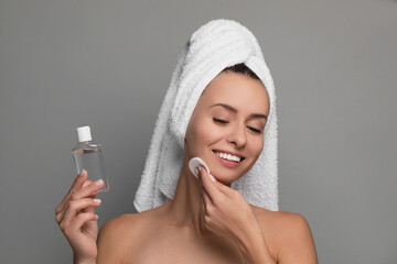 Wall Mural - Smiling woman removing makeup with cotton pad and holding bottle on grey background