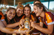 An ecstatic young female rugby team rejoices after a win, muddy and holding a trophy together
