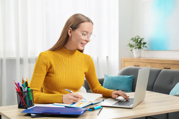 Poster - Woman taking notes while using laptop at wooden table in office