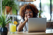 © wolfhound911 - Funny happy smiling African American woman sitting at the desk on workplace at office with juice coctail and booking tickets for summer vacation online via laptop.