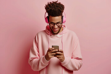 Happy cheerful joyful positive young man on pastel studio background uses mobile phone and noise cancellation headphones head set, listens to music, has good time, enjoys his favorite tracks