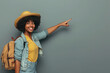 Happy female tourist points at copy space background. Beautiful African American woman with travel bag in casual clothes standing by gray wall, pointing to side and smiling. Holiday trip concept